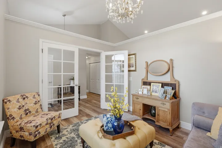 Open-concept living space with vaulted ceilings, a chandelier fixture, recessed lighting, crown molding, and wood-finish flooring