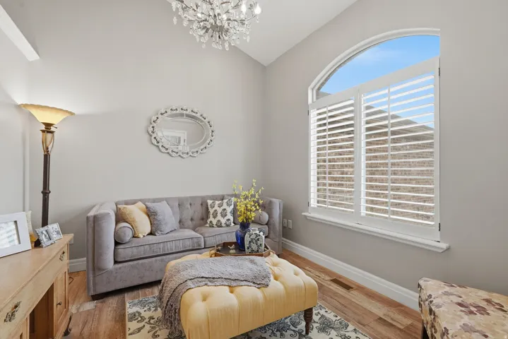 Vaulted ceiling featuring a crystal chandelier, arched window with plantation shutters, wood-finish flooring, and light gray wall paint