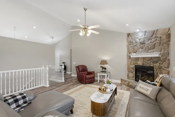 Living area featuring a stone fireplace with a white mantel, high vaulted ceilings, wood-finish flooring, and recessed lighting