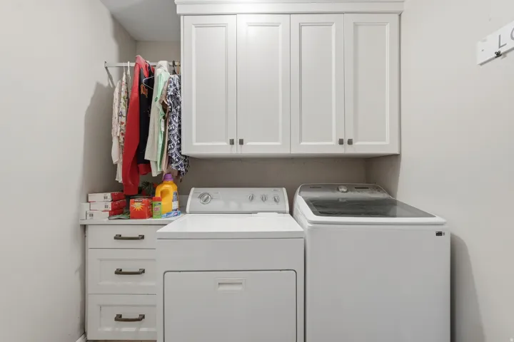 Dedicated laundry area featuring built-in white shaker-style cabinetry, a countertop surface, a hanging rod, and light gray walls