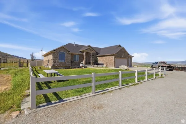 Stone and brick-clad ranch-style residence featuring a two-car garage, dark shingle roofing, and arched window design