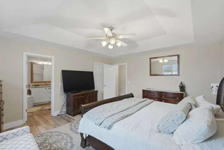 Spacious bedroom featuring a tray ceiling, ceiling fan, and light neutral wall color