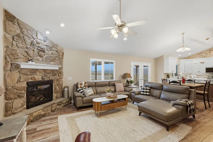 Stone-faced fireplace with a white mantel, vaulted ceiling with recessed lighting and a ceiling fan, wood-finish flooring, and double French doors