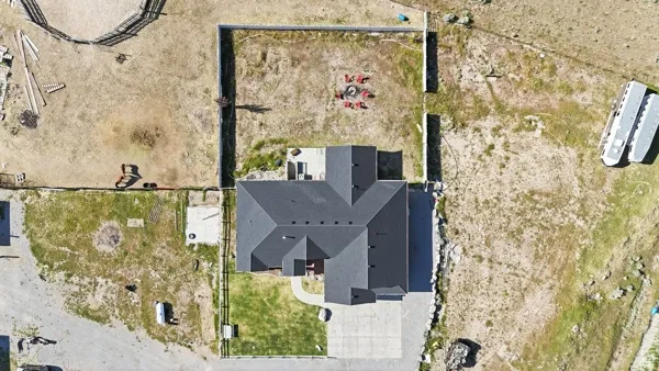 Contemporary residence with a dark shingle roof, a concrete driveway, a paved pathway, a fenced perimeter, and an expansive undeveloped lot