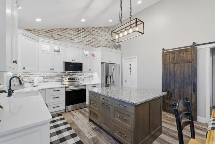 Modern kitchen featuring white cabinetry, stainless steel appliances, a center island with a light-toned countertop, and wood-finish flooring