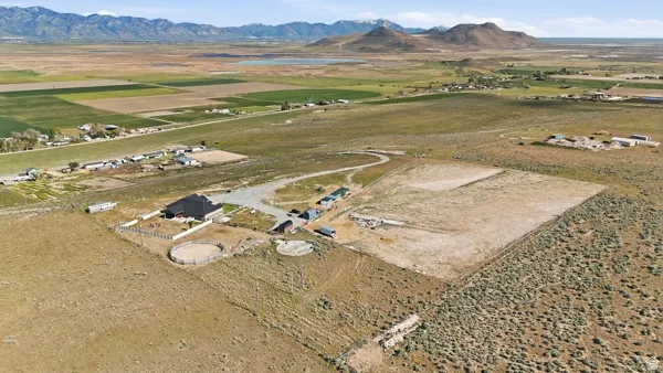 Expansive property featuring a central residence with a dark roof, multiple outbuildings, fenced enclosures, and a circular arena