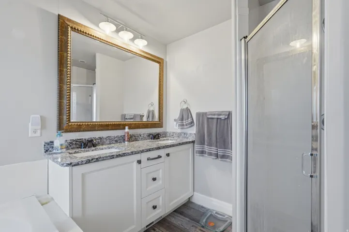 Double vanity with stone countertop, white shaker cabinetry, and dark hardware