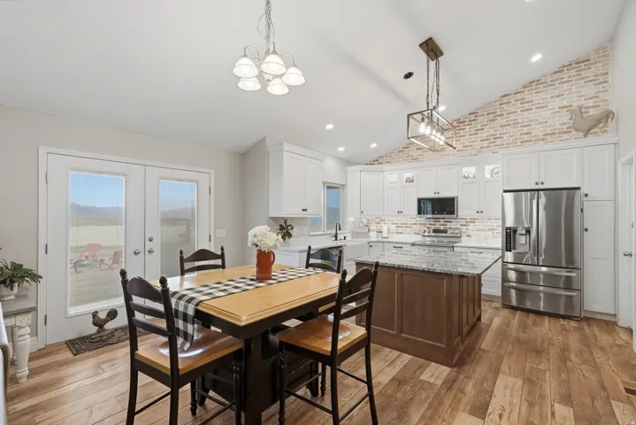Kitchen featuring a vaulted ceiling, wood-finish flooring, white cabinetry, and an exposed brick accent wall