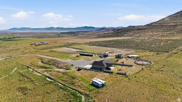 Expansive rural property featuring a main residence with a dark roof, surrounding open land, a circular fenced arena, multiple outbuildings, and a gravel drive