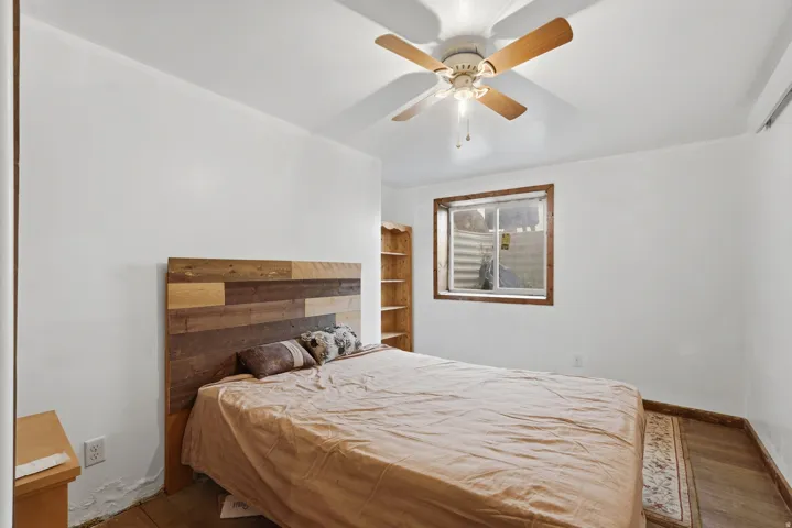 Bright interior room featuring a window with a wood-finish frame, wood-finish flooring, a built-in wood-finish shelving unit, and a ceiling fan with wood-finish blades