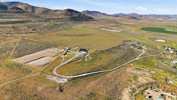 Expansive rural property featuring a paved access road, multiple structures, and varied terrain with established agricultural areas