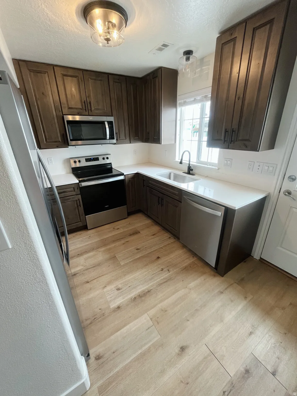 Contemporary kitchen featuring wood-finish flooring, dark wood cabinetry, white countertops, and stainless steel appliances