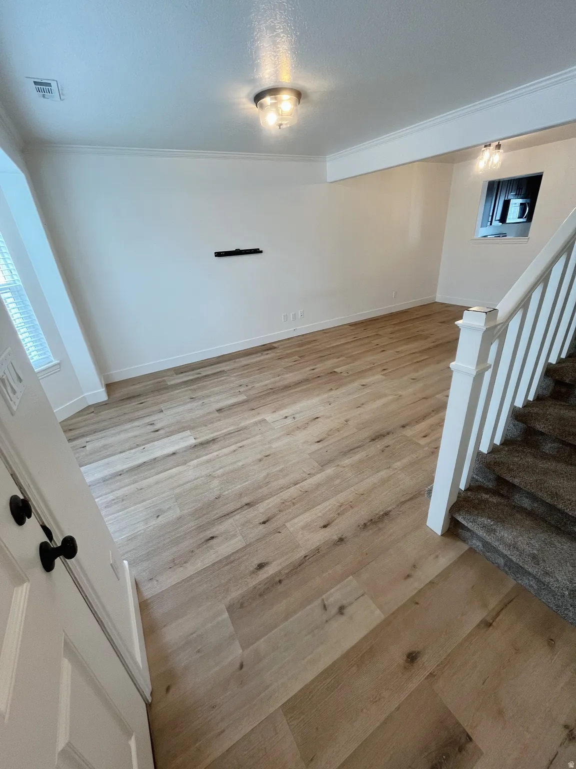 Spacious room featuring wood-finish flooring, white walls, and crown molding