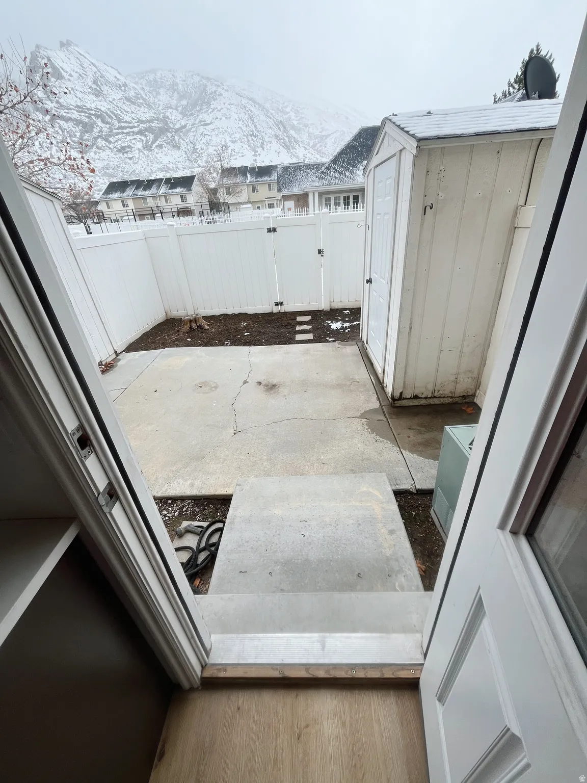 Private concrete patio area featuring a storage shed and white privacy fencing