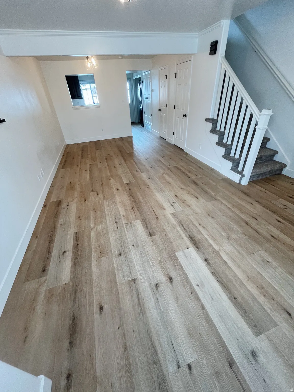 Spacious living room featuring wood-finish flooring, white baseboards, and crown molding
