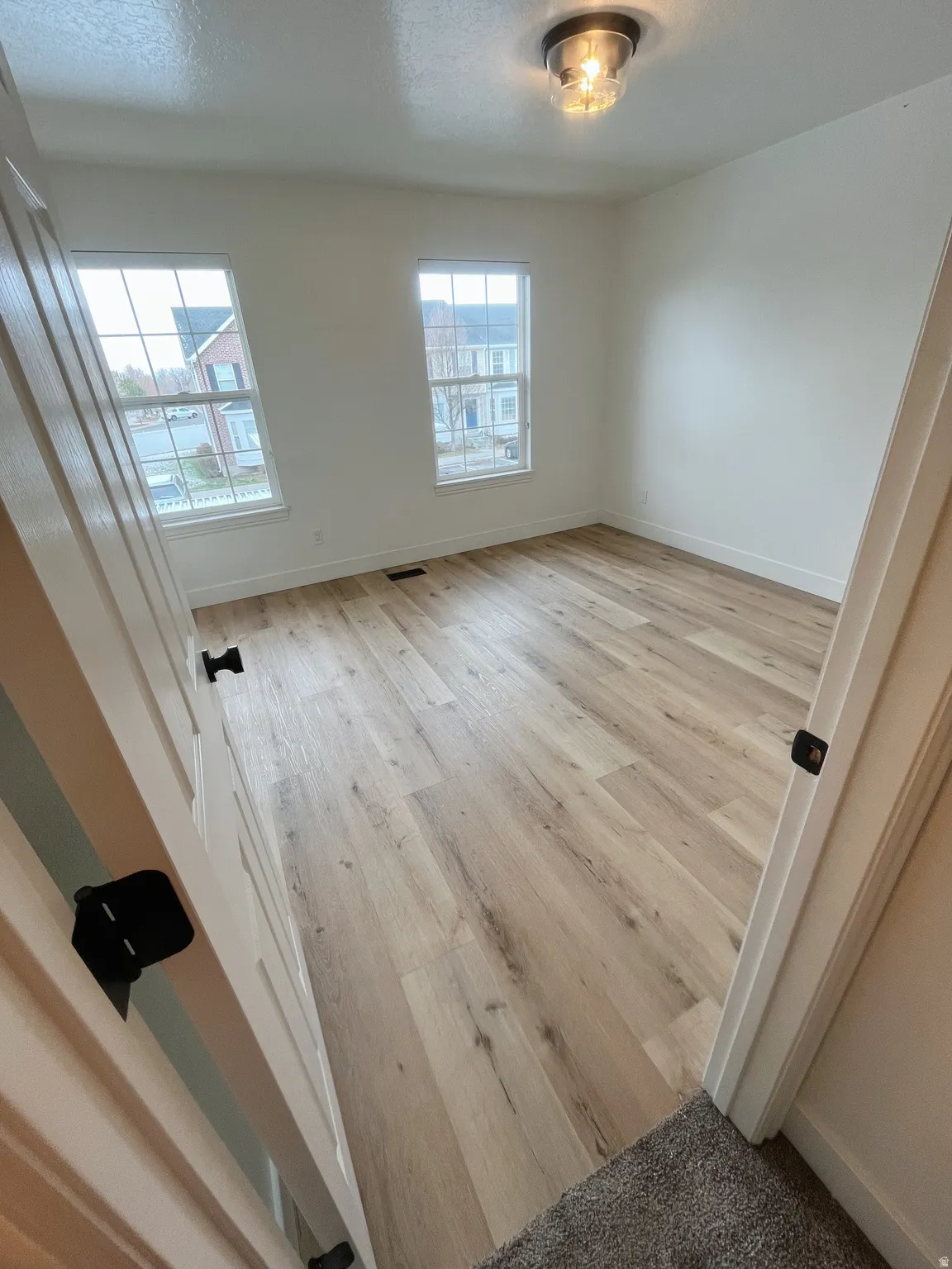 Spacious room featuring light wood-finish flooring, white baseboards, and two double-hung windows