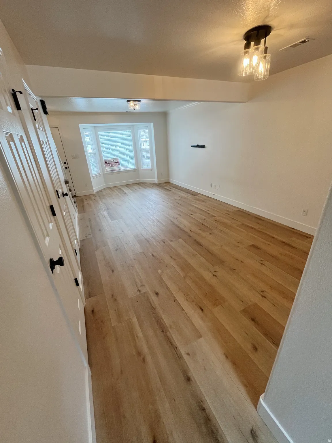 Spacious living room featuring wood-finish flooring, a bay window, and contemporary ceiling lighting