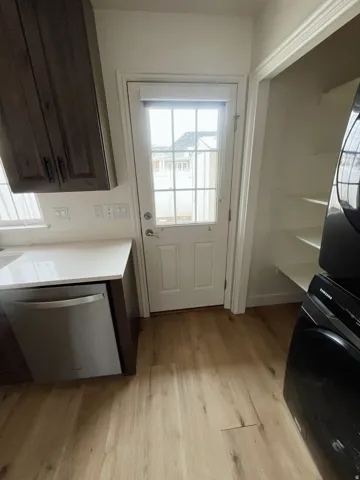 Wood-finish flooring throughout, featuring a full-light paneled exterior door with blinds, dark wood-finish cabinetry, and a built-in stainless steel dishwasher