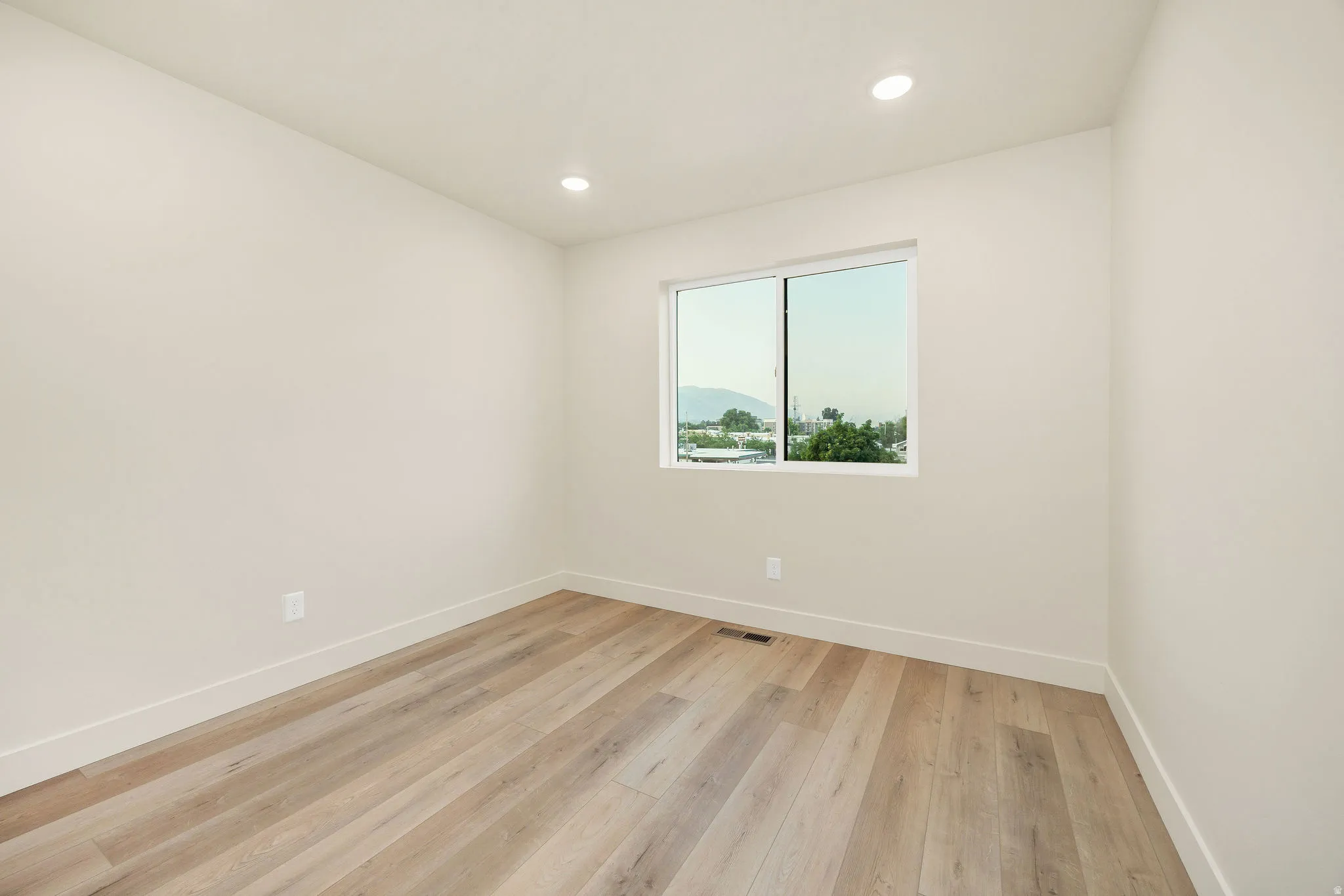Bright room featuring wood-finish flooring, recessed ceiling lighting, a large window, and white baseboards