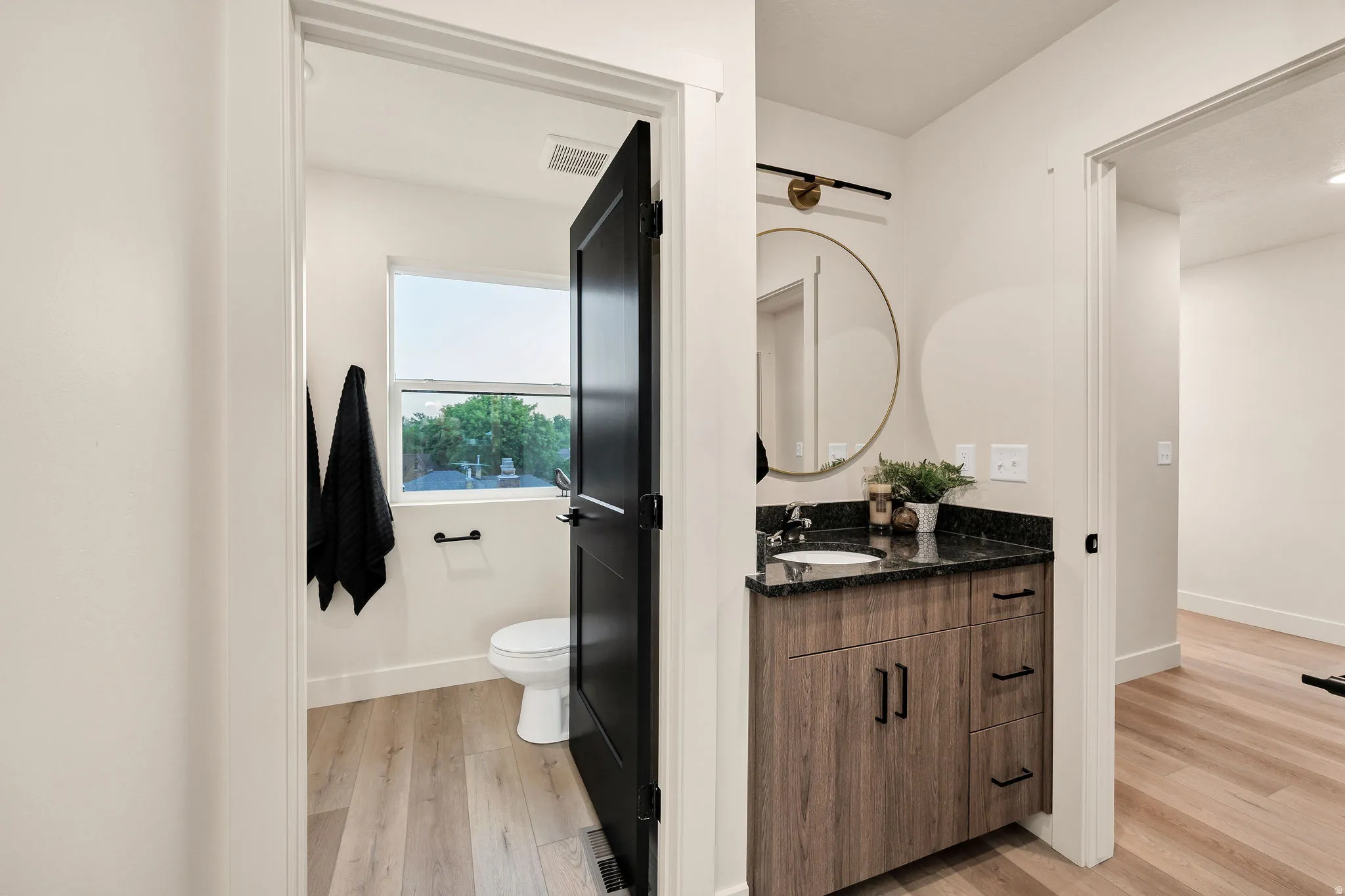 Bathroom vanity featuring a dark granite countertop, undermount sink, and wood-grain cabinetry with matte black hardware