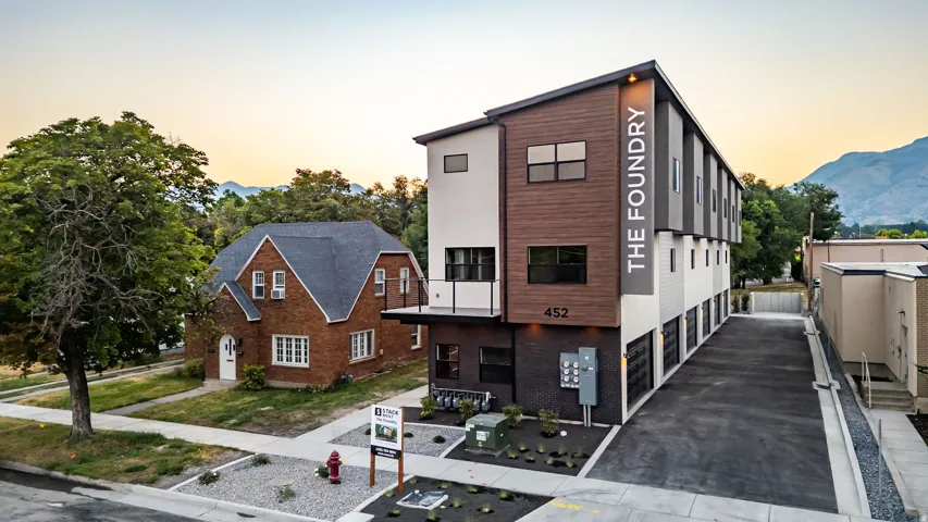 Contemporary multi-story building featuring a multi-textured facade with wood-look siding, white stucco, and dark brick