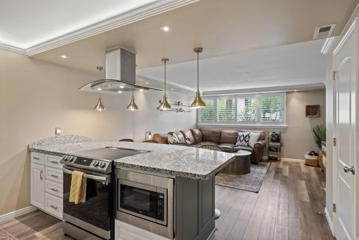 Open-concept living space featuring a kitchen island with built-in microwave and stainless steel range, granite countertops, and pendant lighting