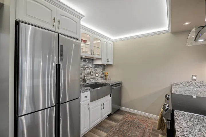 Modern kitchen featuring a stainless steel French door refrigerator, white cabinetry, a farmhouse sink, stone countertops, and a subway tile backsplash