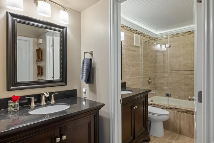 Bathroom featuring a dark wood vanity with a granite-style countertop, an undermount sink, and a framed mirror