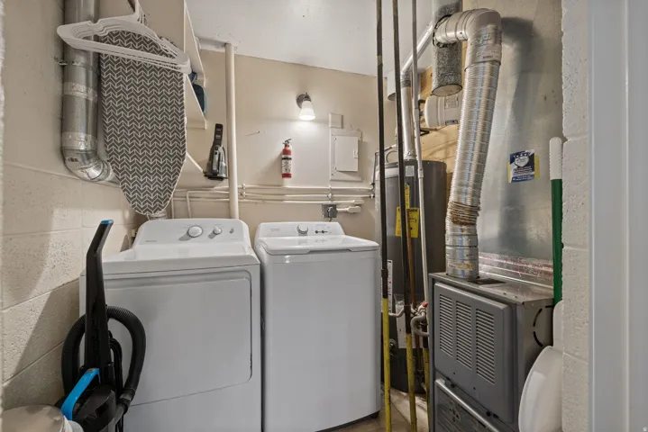Dedicated utility space featuring a washer and dryer, exposed ductwork, wall-mounted lighting, and a water heater