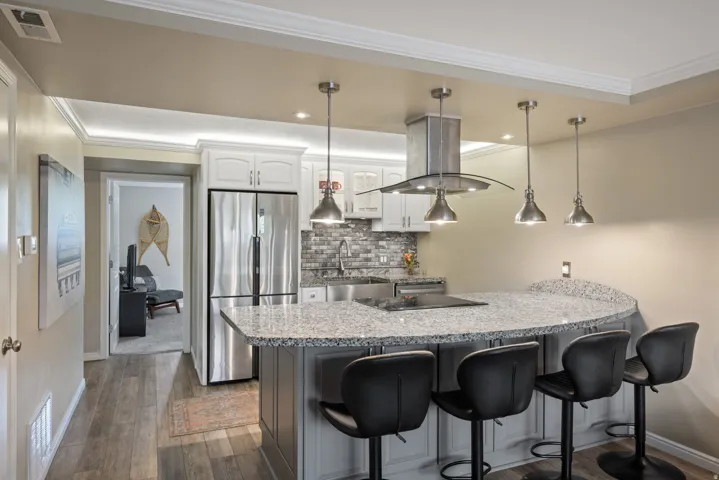 Kitchen featuring a granite-topped island with seating, stainless steel appliances, a tiled backsplash, and recessed and pendant lighting