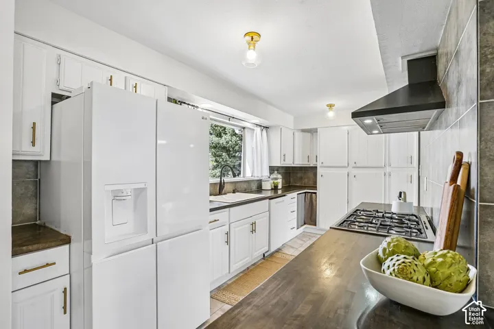 Bright kitchen featuring white cabinetry, brass hardware, dark countertops, a gas cooktop, and a matching black range hood