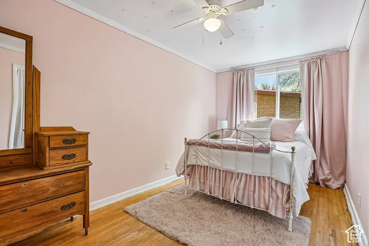Bedroom featuring wood-finish flooring, a ceiling fan with integrated lighting, and a window with a white frame
