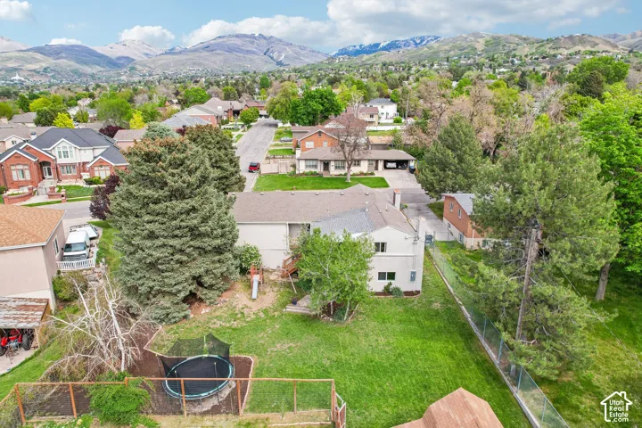 Expansive backyard featuring a manicured lawn, mature trees, and mountainous terrain in the distant background