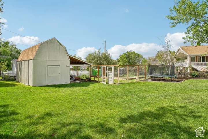 Expansive rear yard featuring a large detached barn-style shed with an attached covered area, a fenced garden plot, and a multi-level deck on the main residence
