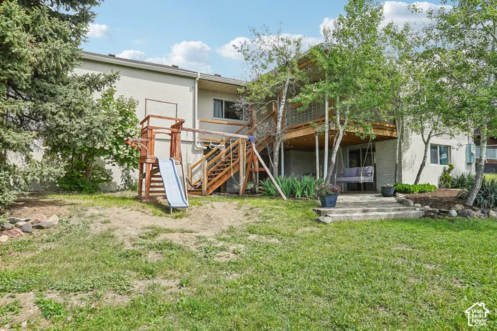 Expansive rear exterior featuring a multi-level wood deck with stairs, a ground-level patio, and mature trees providing natural screening
