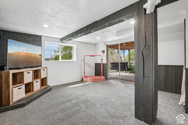 Lower-level room featuring gray carpeting, recessed lighting, and exposed dark wood beams
