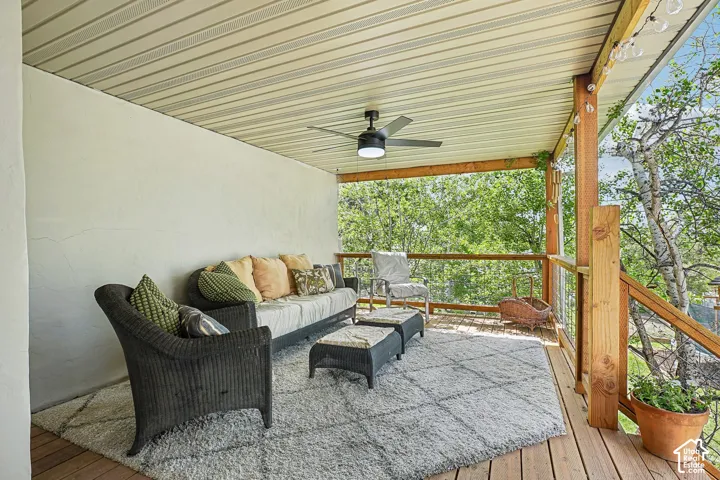 Covered outdoor deck with wood-finish flooring, featuring a ceiling fan with integrated lighting and a wood railing with cable infill