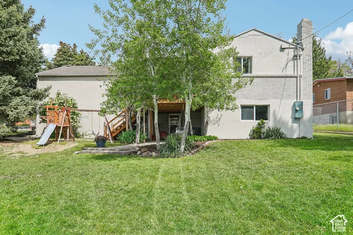 Expansive green lawn with mature trees and a two-story exterior featuring white painted brick and stucco finishes