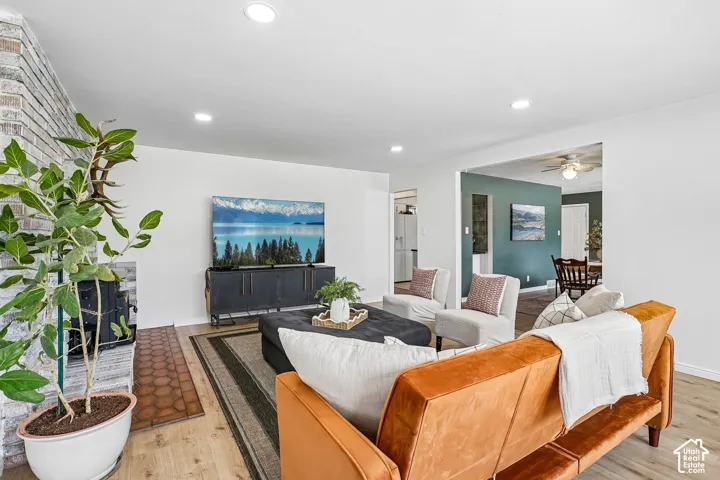 Spacious living area featuring light wood-finish flooring, recessed lighting, and a white brick fireplace with a terracotta tile hearth