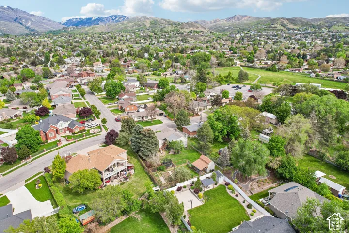 Residential neighborhood with varied architectural styles and mature trees, featuring mountain backdrops, paved streets, and green spaces