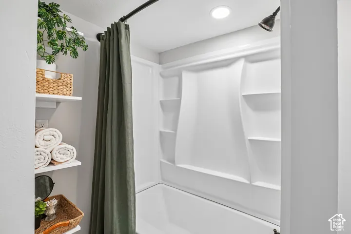White bathtub and shower surround with integrated shelving, matte black shower head, recessed lighting, and built-in shelving
