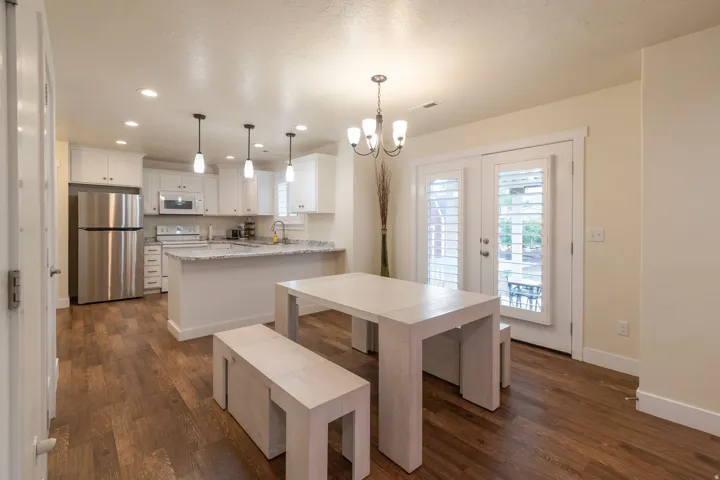 Open-concept kitchen and dining area featuring wood-finish flooring, white cabinetry, a kitchen island with a stone-finish countertop, and stainless steel appliances