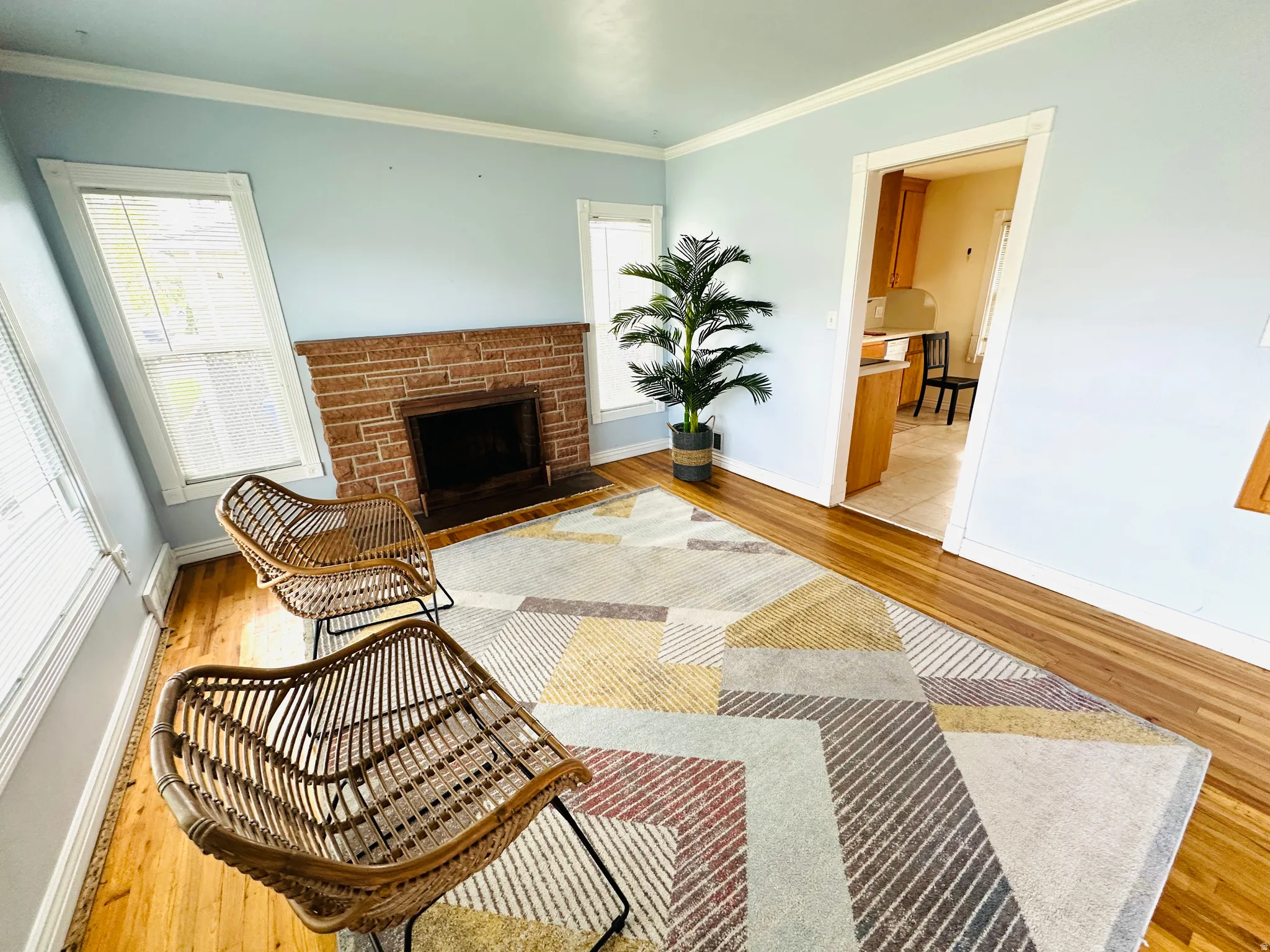 Living area featuring wood-finish flooring, a brick-surround fireplace, light blue wall paint, and white trim