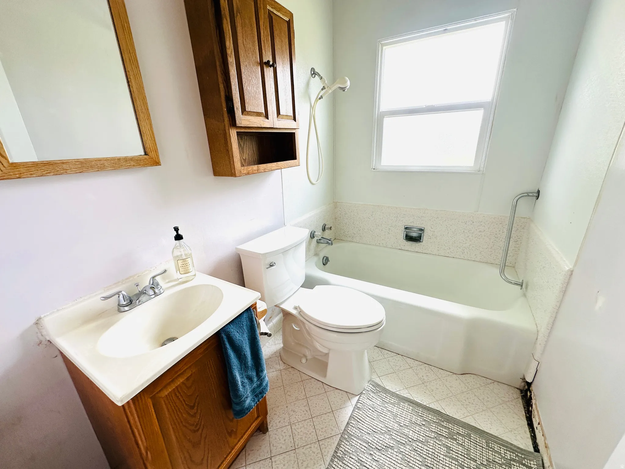 Bathroom featuring a white bathtub with a tiled surround, a window, and an oak-finish vanity with an integrated sink