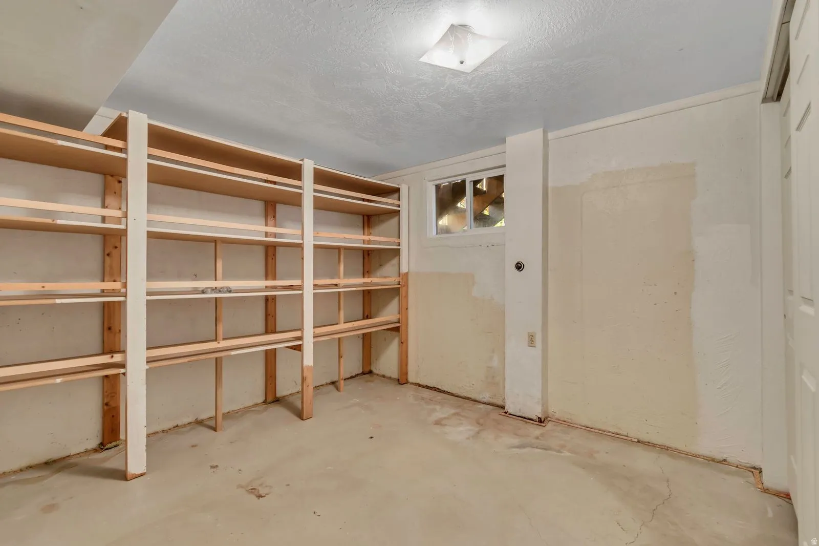 Built-in wood shelving system with multiple tiers, concrete flooring, and a flush mount ceiling light fixture