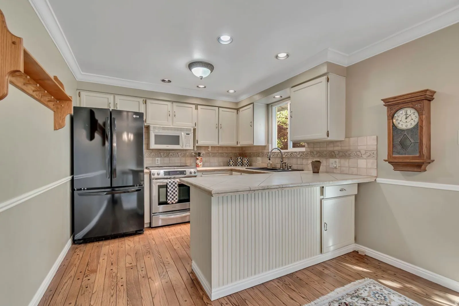 Kitchen featuring wood-finish flooring, white cabinetry, integrated stainless steel appliances, a tiled backsplash, and recessed lighting