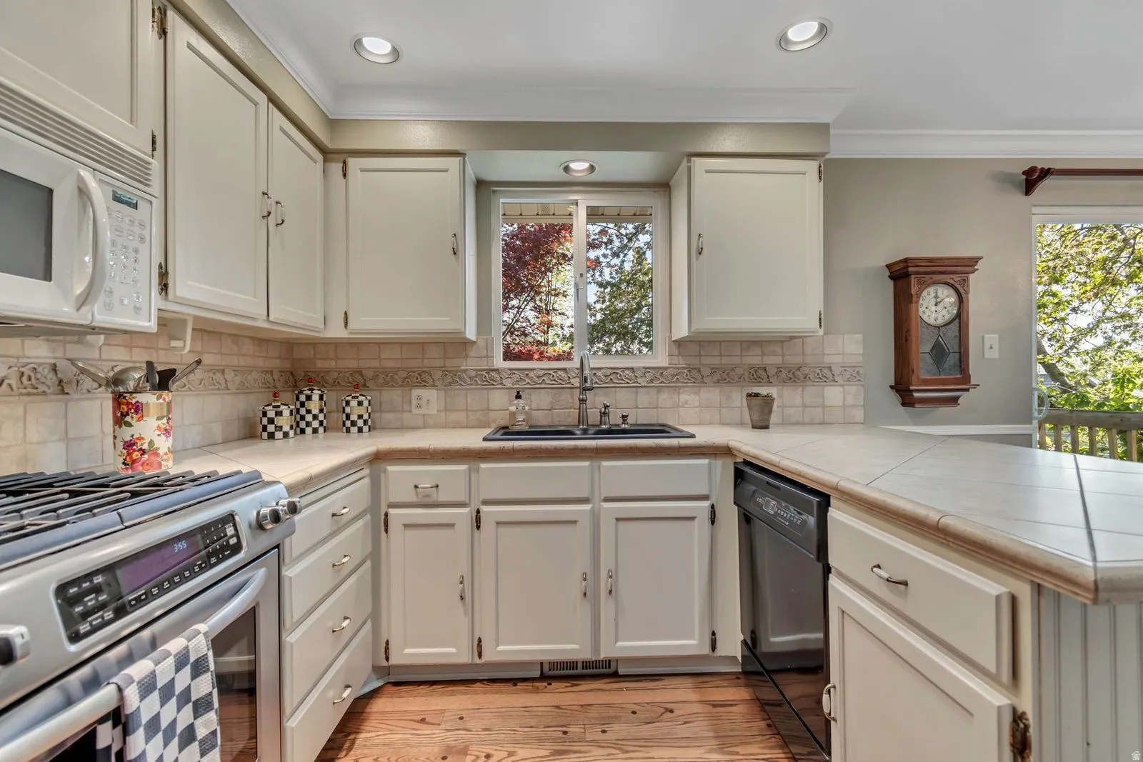 U-shaped kitchen featuring white cabinetry, tile countertops, a stainless steel range, and a built-in dishwasher