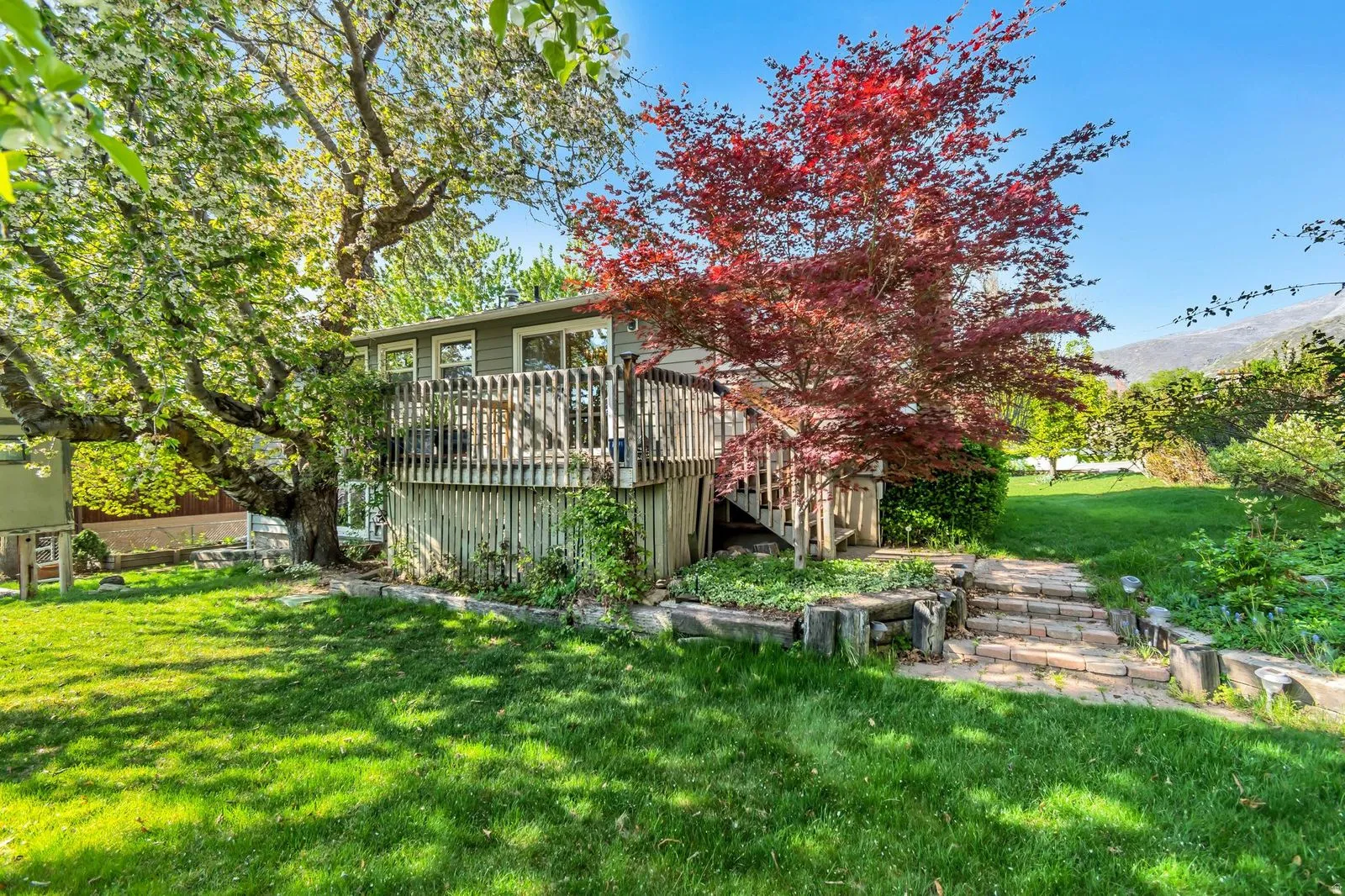 Raised wood deck with privacy railing, accessible via a stone paver pathway and wood stairs