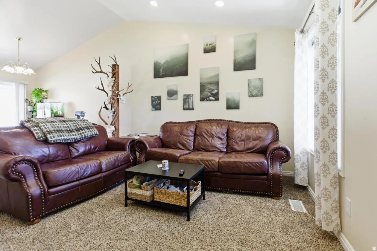 Living area featuring a vaulted ceiling with recessed lighting, neutral wall tones, and a window with patterned drapes