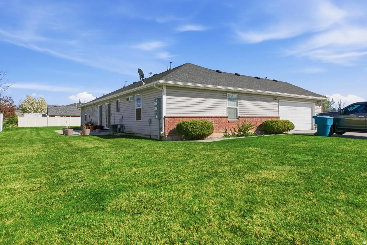 Expansive green lawn surrounds this property featuring light-colored siding and a brick-clad foundation